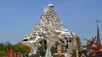 Matterhorn Bobsleds-inspired snowy mountain attraction, with iconic chimneys and alpine rooftops in the foreground, capturing the classic Disneyland adventure experience.