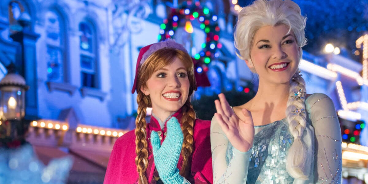 Elsa and Anna from Disney's 'Frozen' film franchise, waving at guests during a Christmas parade at Disney World.