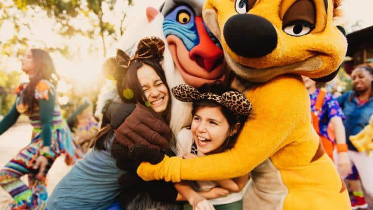 Two girls hugging people wearing Rafiki and Timon costumes