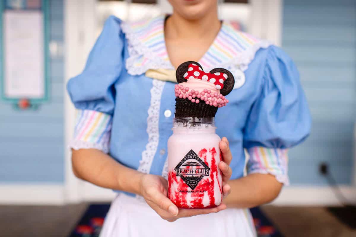 Beaches N Cream Disney World Hostess holding a strawberry freakshake with Minnie cupcake on top