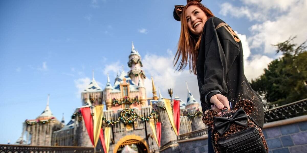 Guest carries Loungefly in front of Sleeping Beauty Castle during Christmas