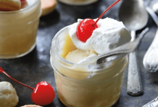 A glass of dessert with cream and a cherry on top