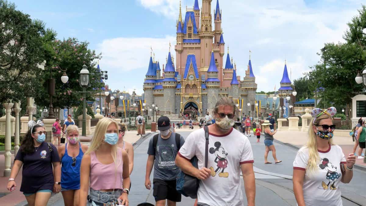 Dozens of Disney World guests walking around Magic Kingdom on a bright, sunny day wearing masks.