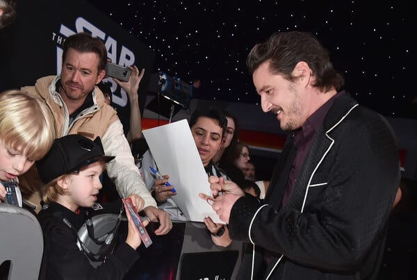 A group of people around each other get an autograph from Pedro Pascal