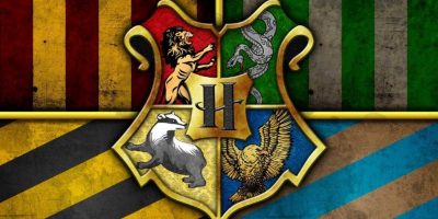 Hogwarts crest featuring the emblems of its four houses: Gryffindor (lion), Slytherin (serpent), Hufflepuff (badger), and Ravenclaw (eagle). The background, symbolizing unity through Hogwarts trauma response, is divided into quarters with each house's colors: red, green, yellow, and blue, separated by gold lines, showing in the new Harry Potter land coming to WB Dubai.