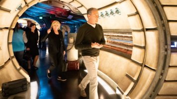 Guests stroll through a dazzling, sci-fi inspired corridor at a Disney park, surrounded by sleek curved walls and vibrant lighting effects, capturing the innovative atmosphere that became iconic under the Iger Era’s leadership.