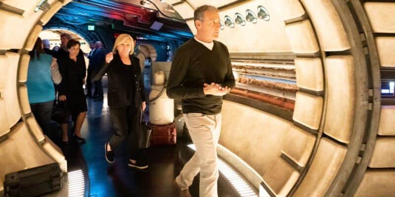 Guests stroll through a dazzling, sci-fi inspired corridor at a Disney park, surrounded by sleek curved walls and vibrant lighting effects, capturing the innovative atmosphere that became iconic under the Iger Era’s leadership.