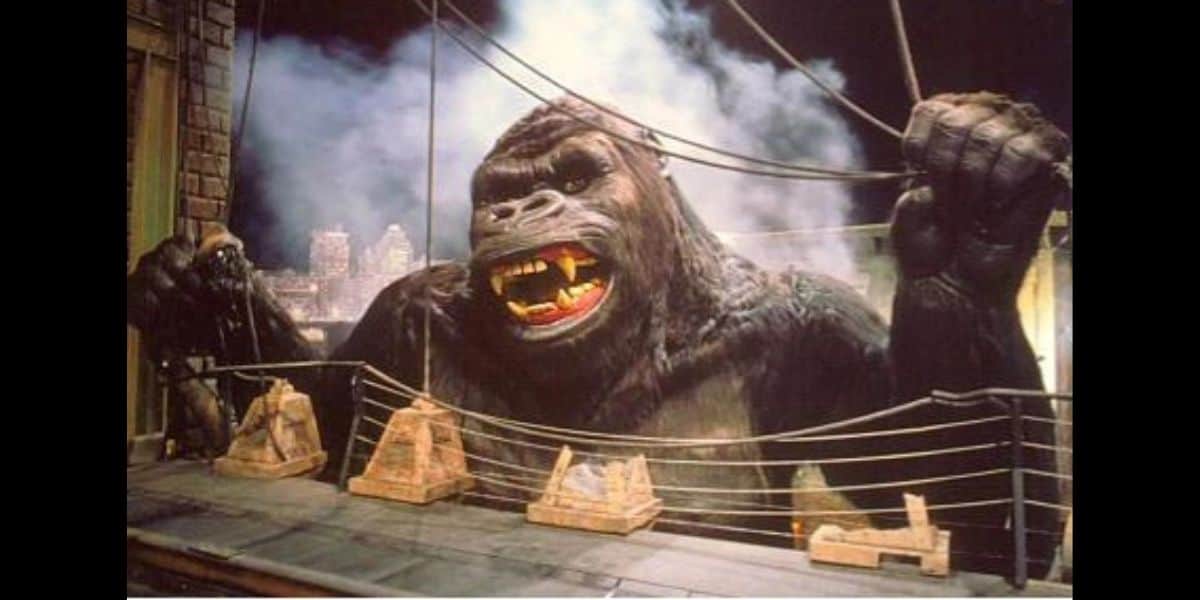 A giant gorilla stands atop a skyscraper, gripping suspension cables and roaring, with a smoky cityscape in the background—evoking the drama of classic monster movies and recalling the Universal King Kong Ride destroyed by fire.