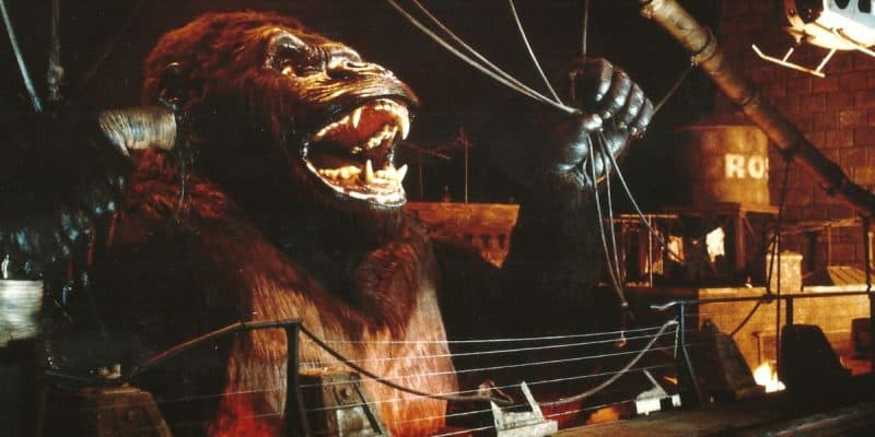 A large animatronic gorilla model, resembling King Kong, roars with mouth open and arms raised, surrounded by set pieces and wires in a dimly lit studio—evoking memories of the Universal King Kong Ride destroyed by fire.