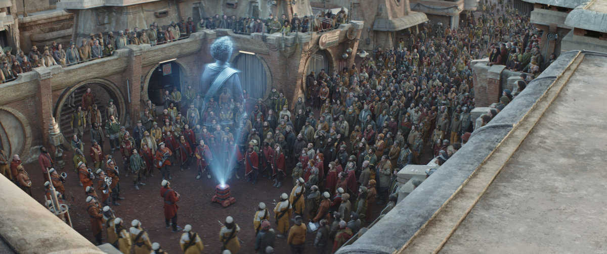 Maarva (Fiona Shaw) and B2EMO surrounded by Ferrixians in a scene from Lucasfilm's ANDOR, exclusively on Disney+. ©2022 Lucasfilm Ltd. & TM. All Rights Reserved.