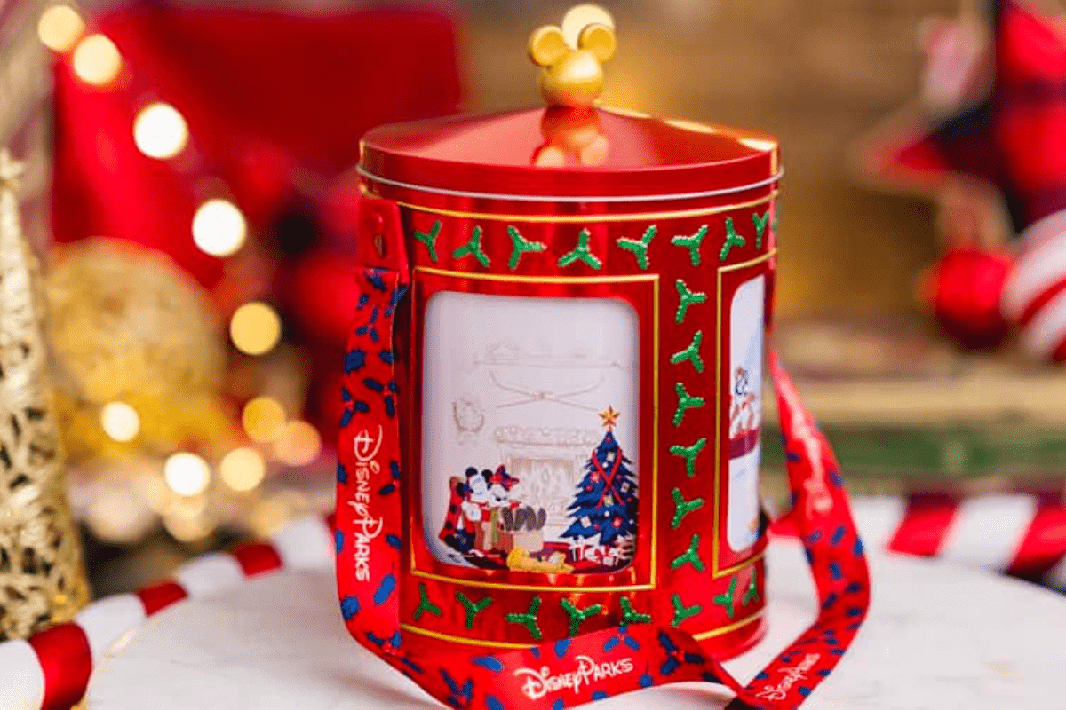 A popcorn tin shaped like a holiday music box, made of a silvery red material with scenes of Disney characters around the Christmas tree painted on the side.