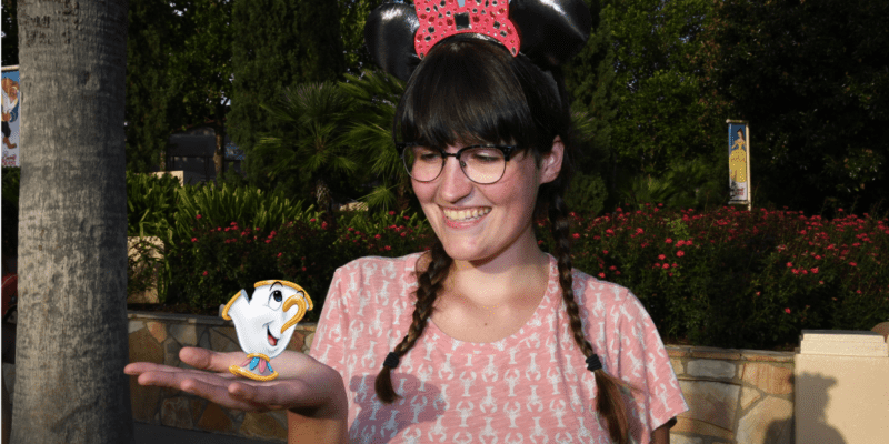 A girl with glasses, brown braids, and black Minnie Mouse ears looks at her hand, where Chip (a teacup) has been added in post-production.