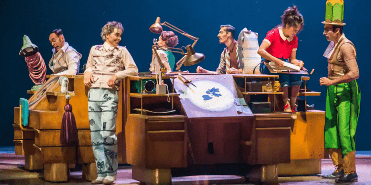 The cast on stage of Cirque Du Soleil, surrounding a drawing desk.