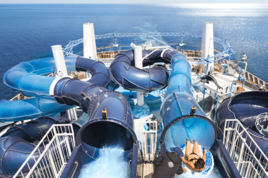 Two blue water slides on the top of a cruise ship. You can see water in the distance.