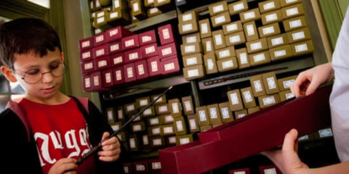 A young boy wearing a 'Harry Potter' robe and glasses selects a wand.