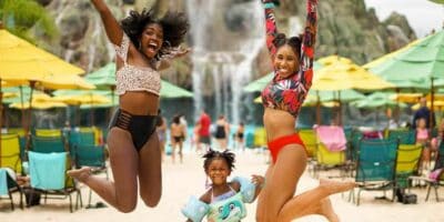 Three girls at Universal Volcano Bay, two jump in the air while a younger one smiles at the camera