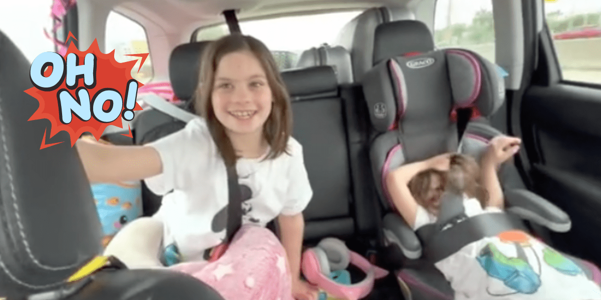 One little girl smiles in the backseat of a car while the other cries and slips out of her seatbelt.