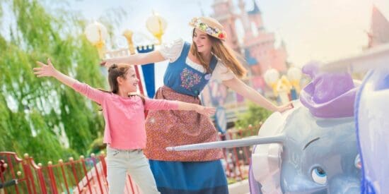 A female Cast Member pretends to fly with a young Guest next to Dumbo