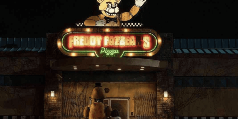 A boy and an animatronic bear stand in front of a withered building with a "Freddy Fazbear's Pizza Place" sign on it