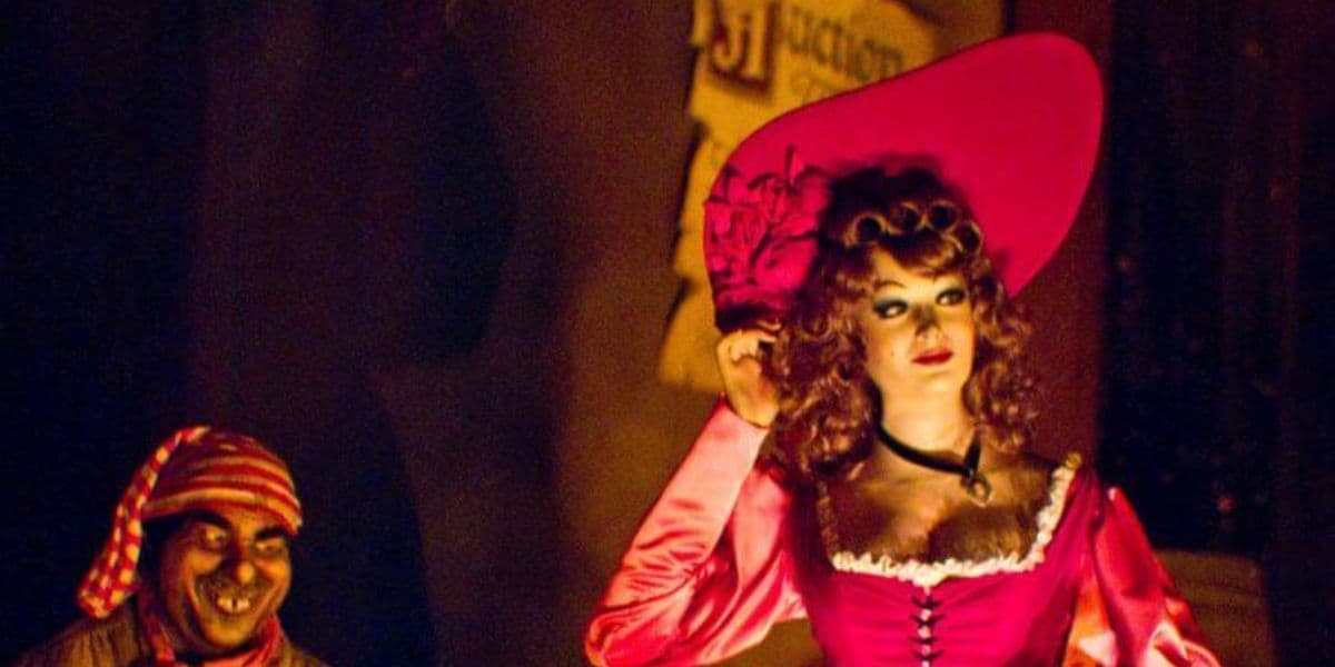 The redhead touches her hat while a pirate watches her