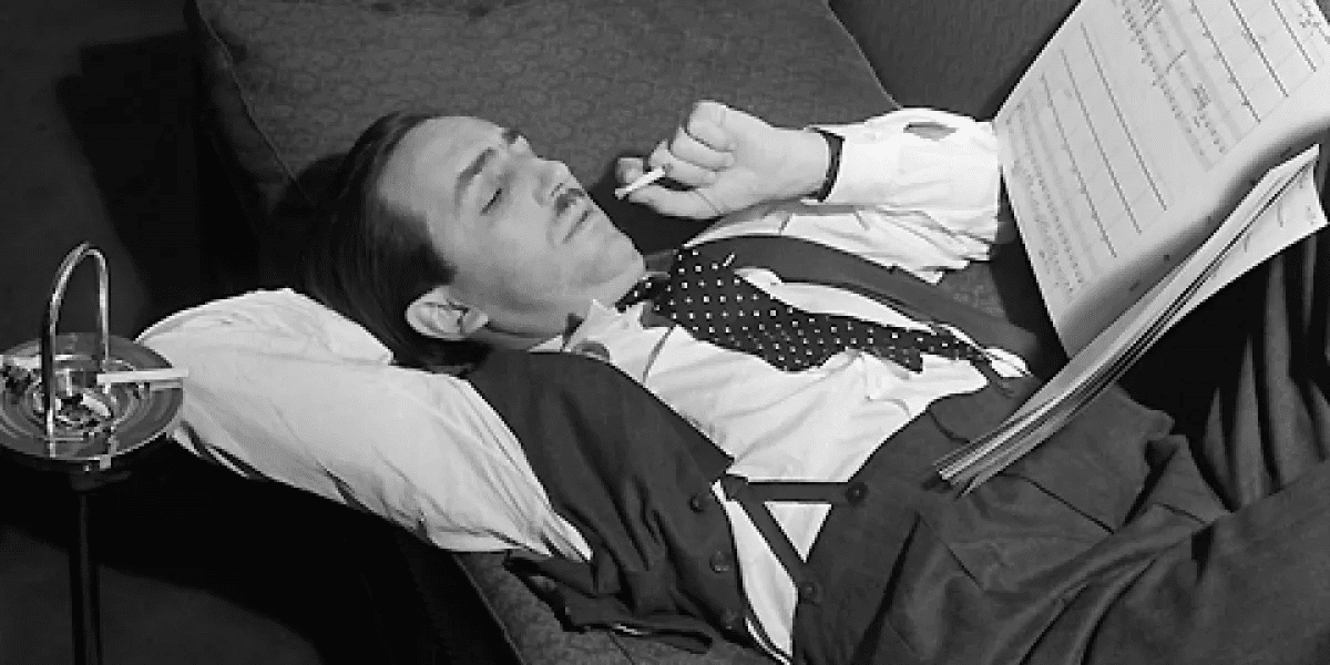 Walt Disney reads a book laying down. He has a cigarette in his mouth.