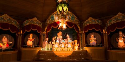 Colorful image of an animatronic stage show featuring Country Bears dressed in country attire, playing musical instruments under warm lighting.