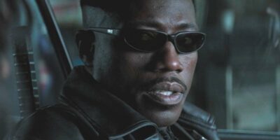 A person wearing black sunglasses and a black leather jacket, channeling MCU Blade vibes, is looking towards the camera. The background is blurred, focusing attention on the person's stern expression.