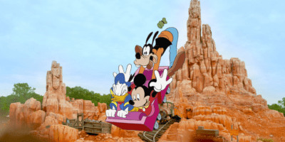 Mickey, Donald, and Goofy on a roller coaster over a photo of Big Thunder Mountain