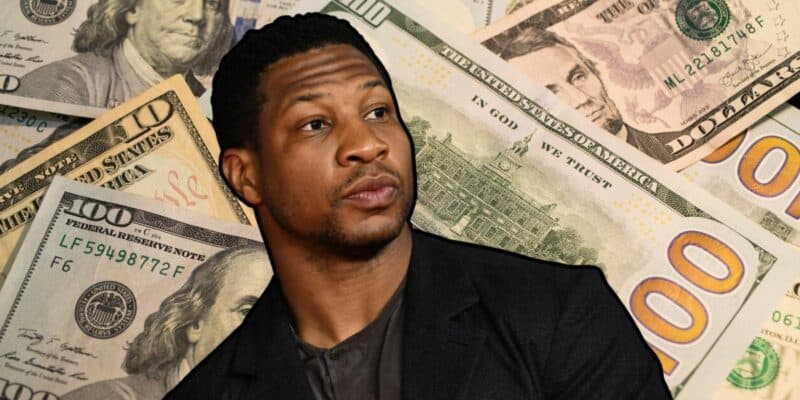 Jonathan Majors posing in front of a pile of money.