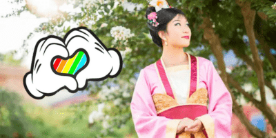 Mulan meeting Guests at EPCOT with Mickey Mouse's hands shaped in a heart wtih an LGBTQIA+ flag inside