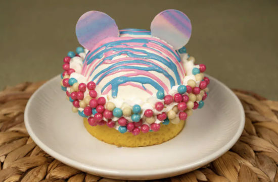A cake with a trans pride flag Mickey head on top.