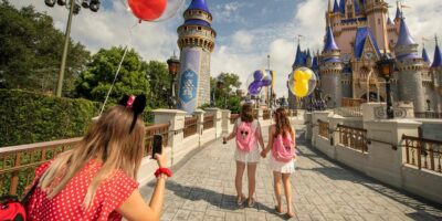 Two little girls walk toward the disney castle, being photographed by a woman in mickey ears. All carry balloons.