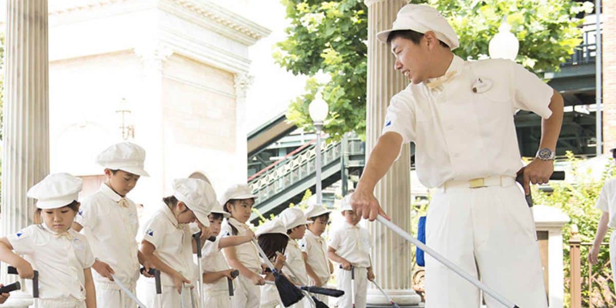 An adult Custodial Cast Member shows children how to sweep