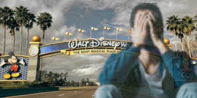 Walt Disney World sign with man holding his face in his hands in foreground
