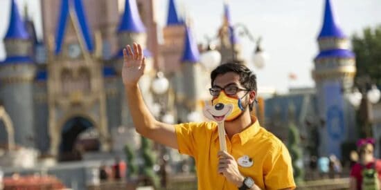 Cast Member wears a mask and holds a Mickey mask in front of their face outside Cinderella Castle