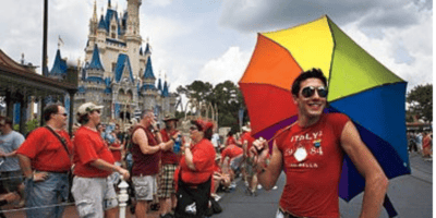 A man in a red shirt holds a rainbow umbrella at Walt Disney World Gay Days.