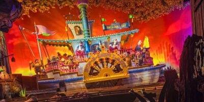 Colorful indoor amusement park ride featuring a pirate ship with cartoon-like characters, vibrant lights, and autumn leaves decoration, creating a whimsical, festive atmosphere at Magic Kingdom.