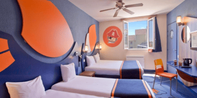 Two beds and a wooden wall console with a mirror and TV at Explorers Hotel.