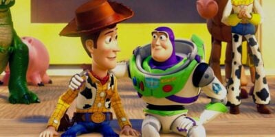 Woody (L) and Buzz (R) sat down looking at each other with other toys in the background