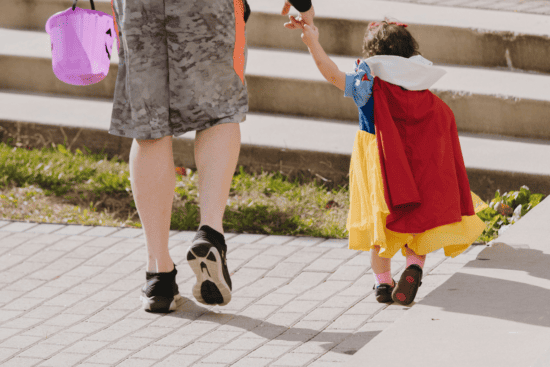 A man holding the hand of a toddler dressed in a Snow White costume while they both walk forward