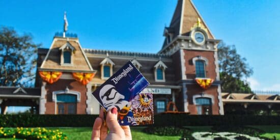 Someone holds up two Disney Park tickets in front of the Disneyland Railroad