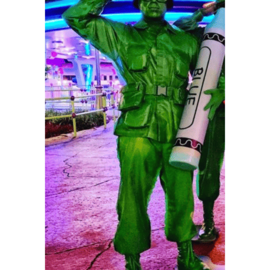 A Disney Character actor, Justin Aldridge, portrays a green army man holding a blue crayon and saluting.