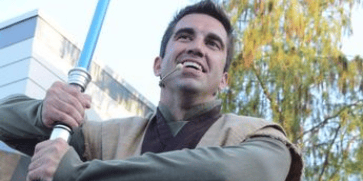 A male Disney Character actor holds a lightsaber.