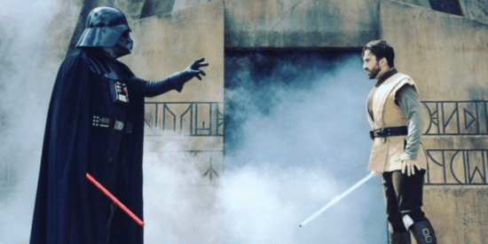 Darth Vader and Justin Aldridge face off with light sabers on stage.