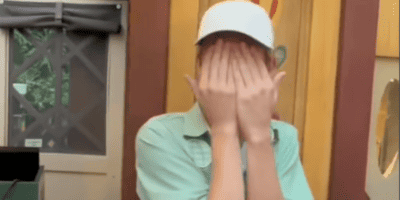 A Disney Cast Member covers his face while being filmed.