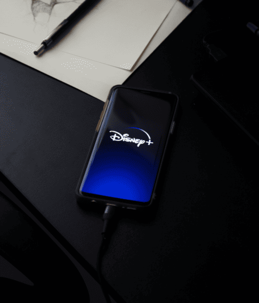 Phone placed on desk while plugged into charger displaying the Disney+ startup screen.