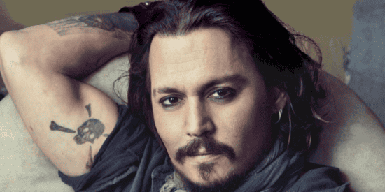Posed photo of Johnny Depp with left arm positioned behind the head, exposing arm tattoos, while he looks directly into the camera