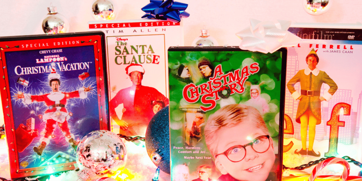 A collection of Christmas movies on display with Christmas ornaments and gift bows. From left to right, the movies displayed are Christmas Vacation, The Santa Clause, A Christmas Story, and Elf