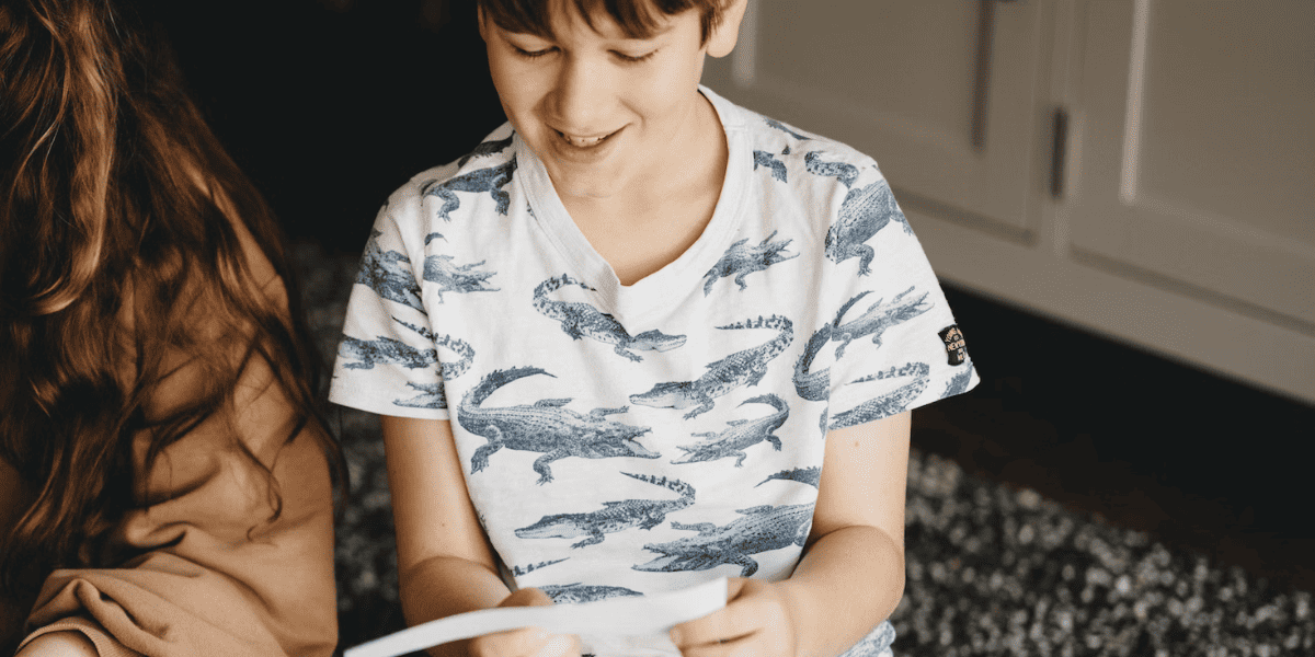 Young boy wearing alligator graphic shirt smiling while reading a small piece of paper