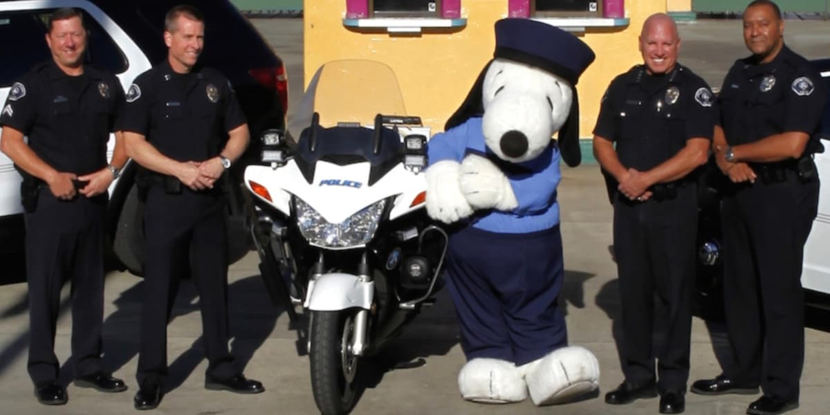 Snoopy dressed as a police officer holding a motorcycle surrounded by other police officers